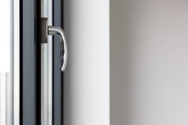 Kamu binasındaki büyük bir pencerenin kolunu eğ ve çevir. Pencere plastik, görünür silikon mühürlerden yapılmış..