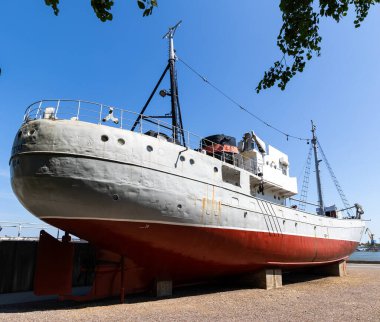 Tarihi bir balıkçı teknesi sudan çıkarıldı ve müzenin rıhtımında sergilendi. Güneşli bir günde, mavi gökyüzüne karşı çekilen bir gemi.