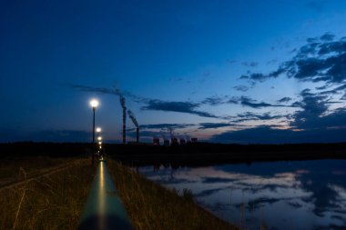 Kömür santralinin gece görüşü. Elektrik santralinin ışıkları göle yansıyor. Yüksek elektrik masrafları. Fotoğraf gece doğal ışıkla çekildi.