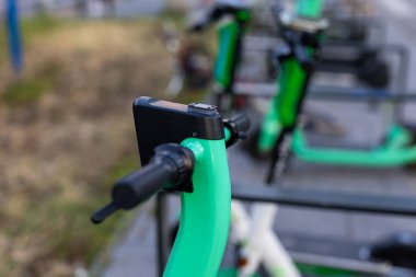 Yeşil elektrikli scooter 'ın gidonuna yakın plan. Arka planda bulanık şehir. Kiralık şehir kişisel taşıma araçları