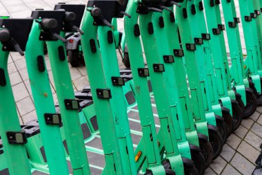 Şehir kaldırımına park edilmiş yeşil elektrikli scooterlar. Kiralık şehir kişisel taşıma araçları