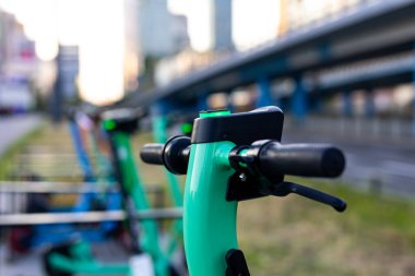 Yeşil elektrikli scooter 'ın gidonuna yakın plan. Arka planda bulanık şehir. Kiralık şehir kişisel taşıma araçları
