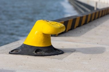 Beton iskelede sarı demirleme kancası. Rıhtıma demirlemiş teknelerin güvenliği. Fotoğraf güneşli bir günde çekildi.