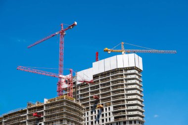 Beton bir apartmanın şantiyesinde inşaat vinçleri. Bina ve vinçler mavi gökyüzüne karşı. Fotoğraf güneşli bir günde çekildi..