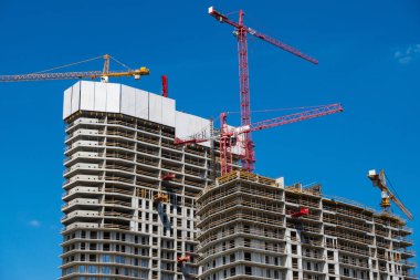 Beton bir apartmanın şantiyesinde inşaat vinçleri. Bina ve vinçler mavi gökyüzüne karşı. Fotoğraf güneşli bir günde çekildi..