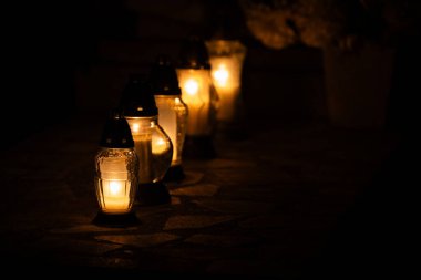 Mezar taşlarının üzerinde duran cam mezarlık mumlarının alevlerinin gece çekimi. Silah sesi Azizler Günü 'nde, 1 Kasım' da çekildi..