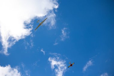 Beyaz planör uçağı diğer küçük uçaklar tarafından mavi gökyüzüne doğru çekiliyor. Güneşli bir günde planör çekiyor.