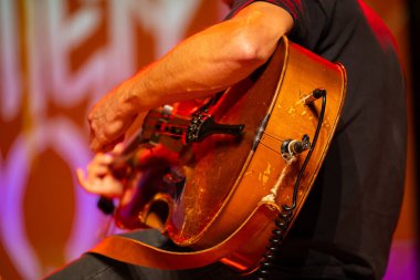 Çello çalan bir çellocu, sahnede alışılmadık bir şekilde çello çalıyor. Fotoğraf konser salonunda yapay ışıkla çekildi.