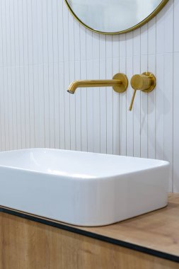Banyodaki bronz banyo musluğu beyaz fayanslarla kaplanmış. Minimalist banyo bitirme. Doğal ışıkla çekilmiş..