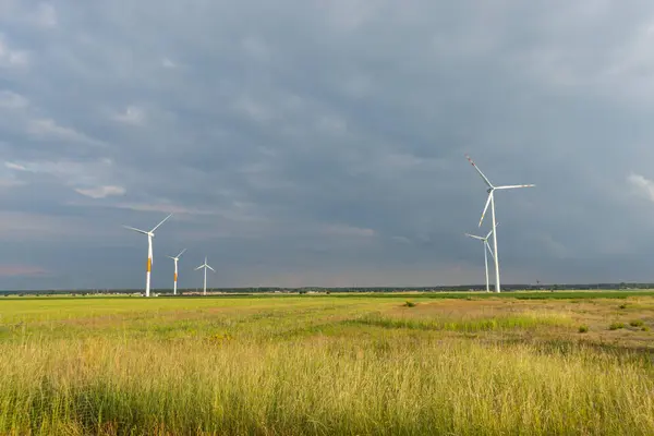 Stock image Distant white wind turbines against a dramatic cloudy sky. Meadow in the foreground, taken late afternoon