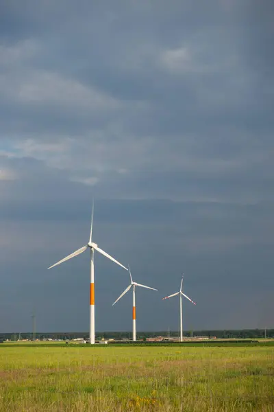 Stock image Distant white wind turbines against a dramatic cloudy sky. Meadow in the foreground, taken late afternoon