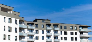 Yeni yapılmış bir apartmanın beyaz ve bej dış cephesi. Binanın üstündeki açık mavi gökyüzü. Fotoğraf güneşli bir günde çekildi.