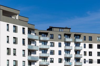Yeni yapılmış bir apartmanın beyaz ve bej dış cephesi. Binanın üstündeki açık mavi gökyüzü. Fotoğraf güneşli bir günde çekildi.