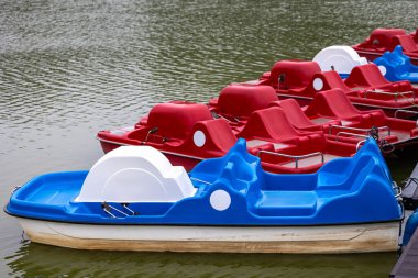 Ahşap iskelenin yanındaki gölete park etmiş kırmızı ve mavi pedallı. Su arıtma ekipmanları harekete hazır.