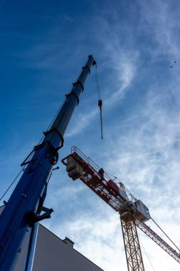 Mobil vinç kullanan bir inşaat vinci. Her iki makinenin gündüz görüntüsü mavi gökyüzüne karşı