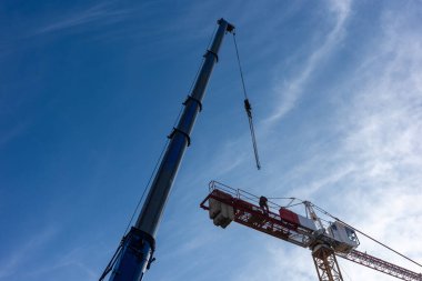 Mobil vinç kullanan bir inşaat vinci. Her iki makinenin gündüz görüntüsü mavi gökyüzüne karşı