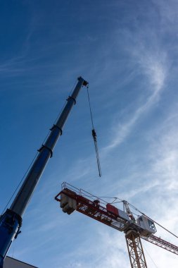 Mobil vinç kullanan bir inşaat vinci. Her iki makinenin gündüz görüntüsü mavi gökyüzüne karşı