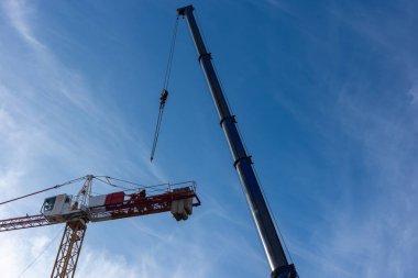 Mobil vinç kullanan bir inşaat vinci. Her iki makinenin gündüz görüntüsü mavi gökyüzüne karşı