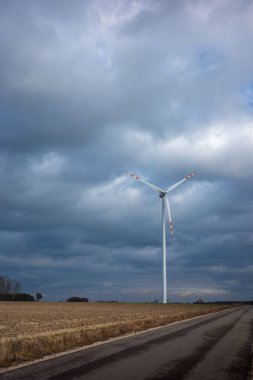 White wind turbine rotor standing on the fields. White clouds and blue sky in the background. clipart