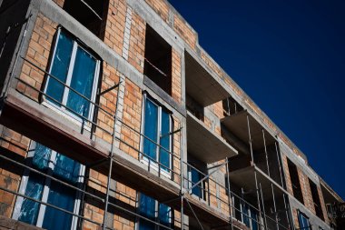 Yeni yapılmış kırmızı tuğlalı bir apartmanın çelik iskelesi. Fotoğraf, mavi gökyüzü ile güneşli bir günde çekildi.. 