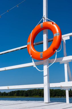 Beyaz iskelenin raylarında asılı turuncu yüzme tekeri. Su kıyısında güvenlik ekipmanları.