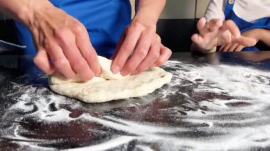 Küçük çocuk evde ekmek pişirmek için annesinin hamur hazırlamasına yardım ediyor. Ev yapımı ekmek. El yapımı hamur. Ev konseptinde yemek yapmak. Aile kavramı.