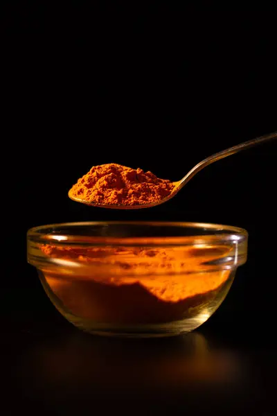 İçinde zerdeçal tozu olan bir kase. Siyah arka planda zerdeçal baharatı. Bir kaşık baharat. Yemek için çeşni.