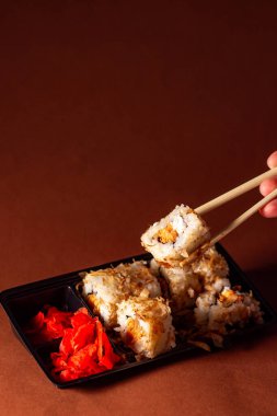 Çubuklar suşi rulosundan porsiyon alıyor. Suşi, somon krem peyniri ve salatalık paketinde. Yiyecek teslimatı kavramı.