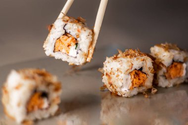 Çubuklar suşi rulosundan porsiyon alıyor. Somon krem peynirli ve salatalıklı suşi. İzole edilmiş. Gri arkaplanda suşi yuvarlanıyor.