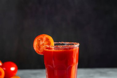 Koyu gri arka planda sallanan sebze kokteyli. Kırmızı domates kokteyli. Domates dilimiyle servis edilmiş. Vegan menüsü.