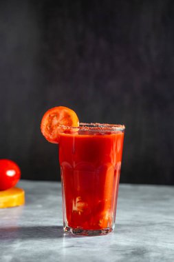 Koyu gri arka planda sallanan sebze kokteyli. Kırmızı domates kokteyli. Domates dilimiyle servis edilmiş. Vegan menüsü.