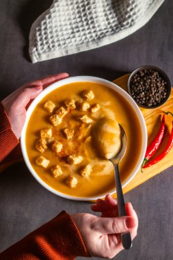 Bir kadın kaşıkla balkabağı çorbası tadıyor. Krema çorbası içiyorum. Yüksek açı. Çorba kasesi, biber, kırmızı biber, tuz servis edildi..