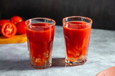 İki sebze, koyu gri arka planda cam içinde sallanmış kokteyller. Kırmızı domates kokteyli. Domates dilimiyle servis edilmiş. Vegan menüsü.