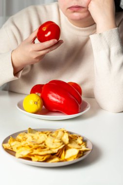 Diyet yapmaktan bıkmış bir kadın. Sıkıcı sağlıklı yiyecekler. Sebze ve kızarmış cips arasında seçim yapan kilolu bir kadın. Kilo kaybı ve diyet konsepti.