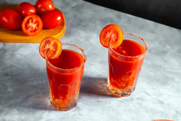 İki sebze, koyu gri arka planda cam içinde sallanmış kokteyller. Kırmızı domates kokteyli. Domates dilimiyle servis edilmiş. Vegan menüsü.