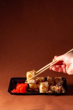 Elleri çubuklu suşi rulosunun bir kısmını alıyor. Suşi, somon krem peyniri ve salatalık paketinde. Yiyecek teslimatı kavramı.