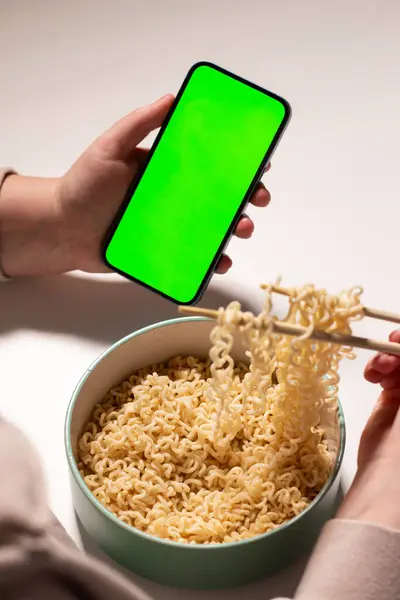 Evde makarna yerken akıllı telefon kullanan bir kadın. Mesaj için yeri olan yeşil ekranlı akıllı telefon. Arka planda servis tablosu olan akıllı telefon ellerinde
