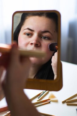 Millennial Kafkas kadınının makyaj tozu sürerken aynaya baktığı dikey görüntüsü. Aynadaki yansıma. Hazırlanıyor. Güzellik konsepti.