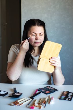 Millennial Kafkas kadınının aynaya bakarken yüzüne makyaj fırçası sürerek makyaj yaptığı dikey görüntüsü. Hazırlanıyor. Güzellik konsepti.