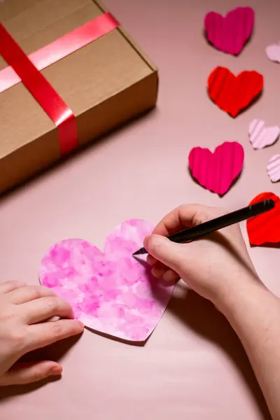 Kadının pembe sevgililer günü kartı yarattığı dikey çekim. Sevgililer günü kartı. Pembe arka planda kalp şeklinde bir kart. Sevgililer Günü konsepti.