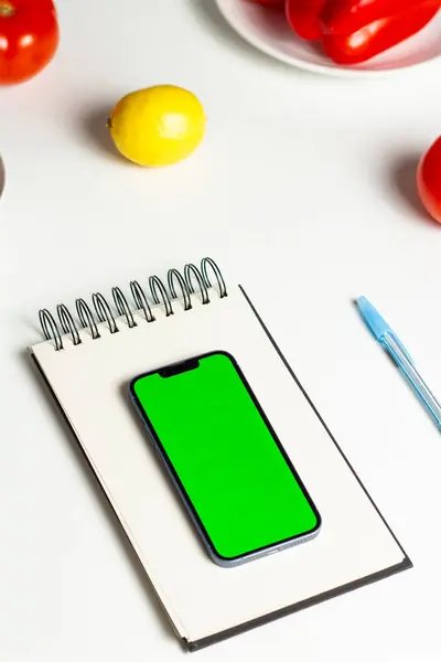 Akıllı telefonda sağlıklı beslenme planı oluşturuyorum. Beslenme planı. Telefondaki yeşil ekran, online kilo verme programı için hazırlanıyor. Defter, sebze ve telefon düzlüğü.