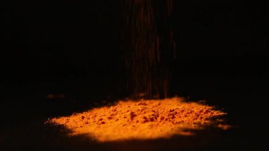 Bir yığın zerdeçal tozu. Siyah arka planda zerdeçal baharatı. Bir kaşık baharat. Yemek için çeşni.