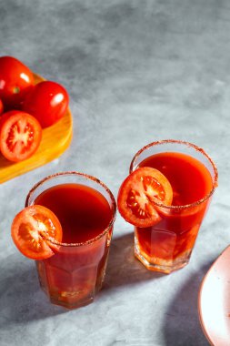 Koyu gri arka planda cam içinde sallanan iki sebze kokteylinin üst görüntüsü. Kırmızı domates kokteyli. Domates dilimiyle servis edilmiş. Vegan menüsü.