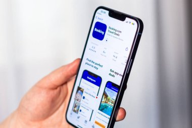 Kaliningrad, Rusya 14.01.25 - iPhone 'u tutan ve uygulama mağazasından Booking.com uygulaması indiren kadın. Daire ve otel araması. Seyahat planlama kavramı.