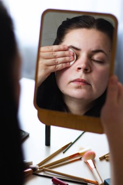 Millennial Kafkas kadınının aynaya bakarken yüzünden makyajı çekerken dikey görüntüsü. Aynadaki yansıma. Yatmaya hazırlanıyorum. Kişisel bakım güzellik konsepti.