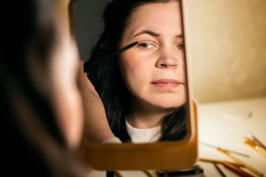 Evde makyaj yapan bir kadın. Rimel sürüyorum. Aynaya bakıyorum. Etkinliğe hazırlanıyorum. Aynadaki yansıma. Güzellik konsepti.