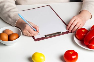 Beslenme planı ve diyet menüsünün boş taklidi. Sebze ve yumurtaların olduğu masada fotokopi alanı olan kağıt. Sağlıklı yemek hazırlayan kadın.
