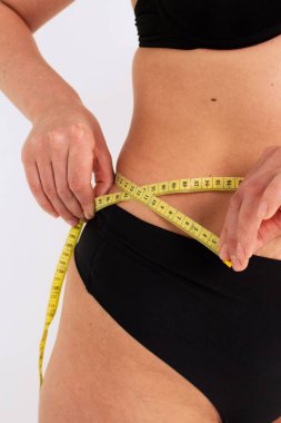 Aşırı kilolu bir kadın vücudunu mezurayla ölçer. Kilo alma ve kilo verme kavramı. Mükemmel kadın vücut konsepti.