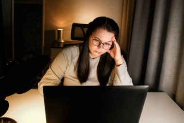 Gözlüklü genç bir kadın gece geç saatlerde evde bilgisayar başında çalışıyor, modern teknolojileri kullanıyor ve çevrimiçi eğitim alıyor. Uzaktan öğrenme konsepti. Online üniversite. Sürece odaklan.