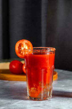 Koyu gri arka planda sallanan sebze kokteyli. Kırmızı domates kokteyli. Domates dilimiyle servis edilmiş. Vegan menüsü.